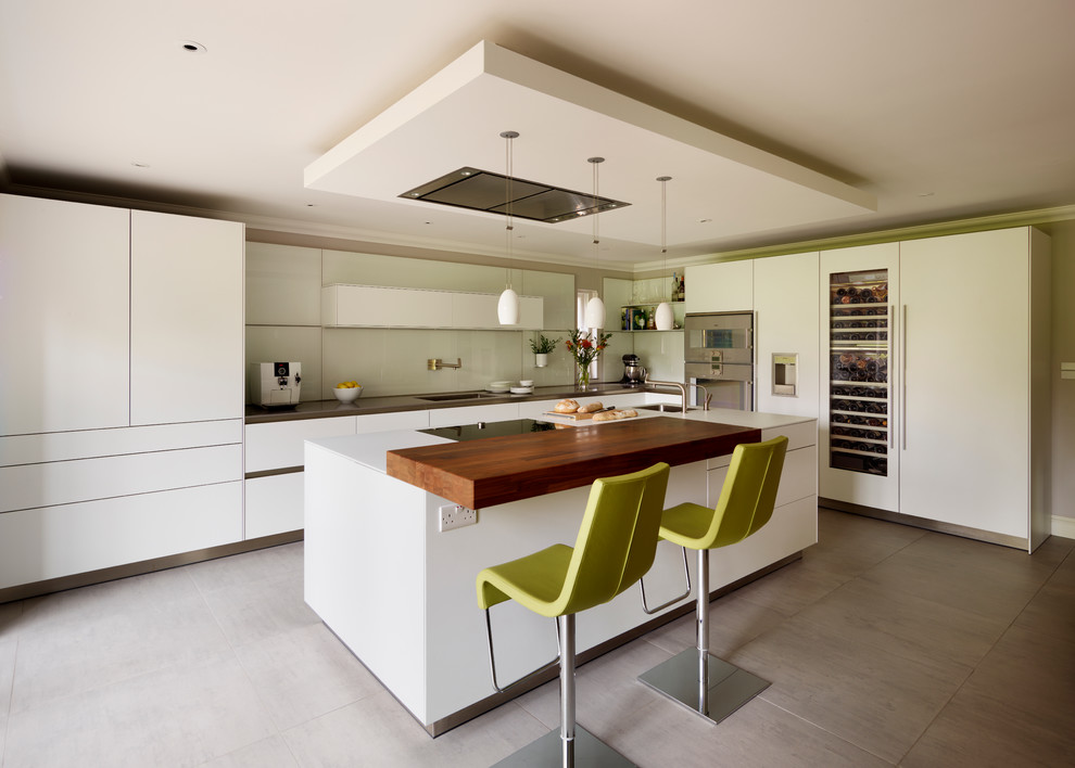 Example of a large trendy l-shaped ceramic tile eat-in kitchen design in Surrey with flat-panel cabinets, white cabinets, quartz countertops, white backsplash, glass sheet backsplash, stainless steel appliances and an island