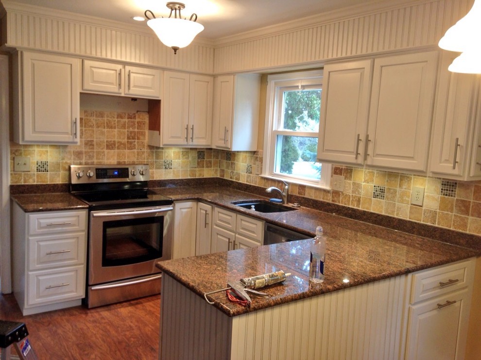 This is an example of a medium sized u-shaped kitchen/diner in Philadelphia with a submerged sink, raised-panel cabinets, yellow cabinets, granite worktops, beige splashback, ceramic splashback, stainless steel appliances, dark hardwood flooring and a breakfast bar.