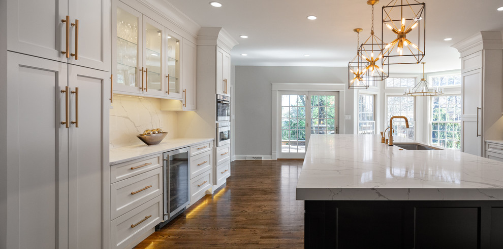 Inspiration for a large transitional u-shaped medium tone wood floor and brown floor kitchen remodel in Other with an undermount sink, flat-panel cabinets, black cabinets, quartz countertops, white backsplash, stone slab backsplash, stainless steel appliances, an island and white countertops