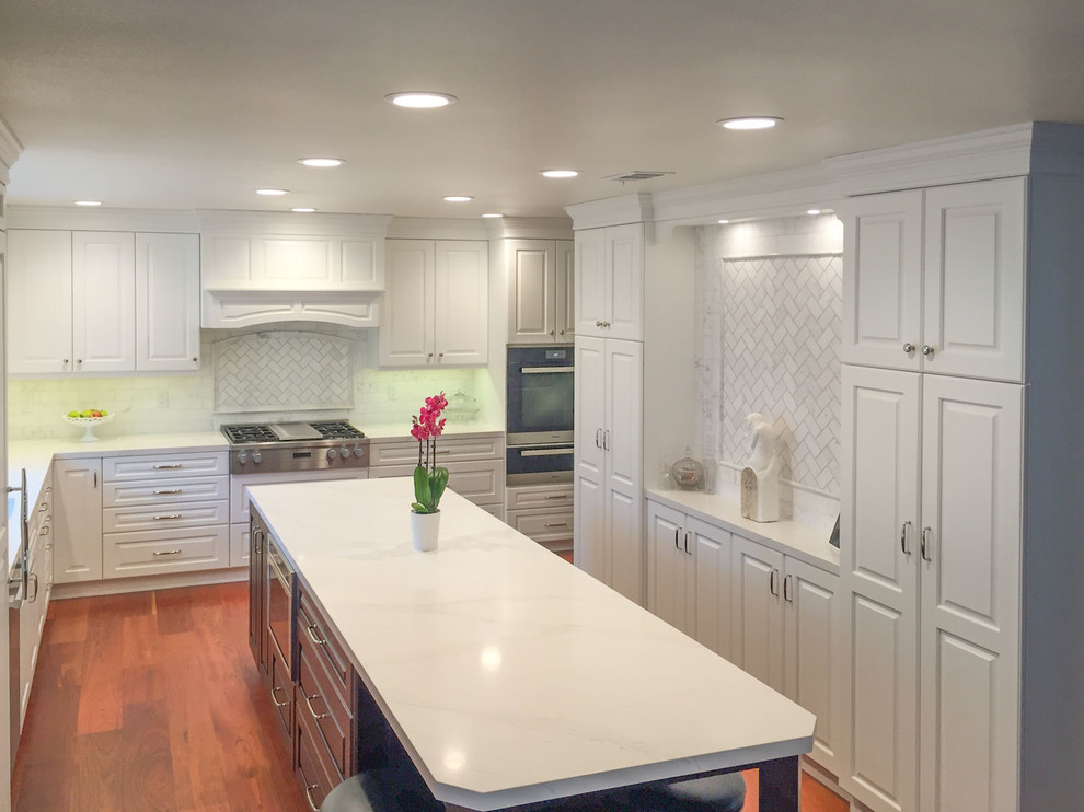 Exempel på ett mellanstort klassiskt vit vitt kök, med en undermonterad diskho, luckor med upphöjd panel, vita skåp, bänkskiva i kvarts, beige stänkskydd, rostfria vitvaror, mellanmörkt trägolv, en köksö och brunt golv