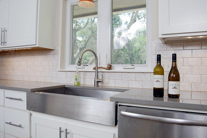 Foto på ett mellanstort funkis kök, med en rustik diskho, skåp i shakerstil, vita skåp, bänkskiva i återvunnet glas, vitt stänkskydd, stänkskydd i tunnelbanekakel, rostfria vitvaror, en köksö och betonggolv