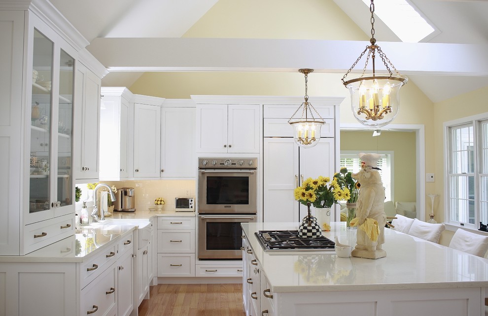 Large transitional l-shaped light wood floor eat-in kitchen photo in Philadelphia with a farmhouse sink, shaker cabinets, white cabinets, quartz countertops, white backsplash, ceramic backsplash, stainless steel appliances and an island