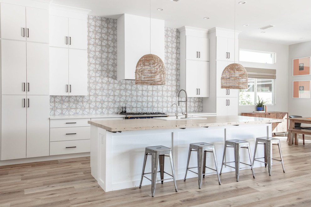 Photo of a large contemporary open plan kitchen in Phoenix with a built-in sink, flat-panel cabinets, white cabinets, wood worktops, multi-coloured splashback, cement tile splashback, stainless steel appliances, light hardwood flooring, an island, beige floors and beige worktops.