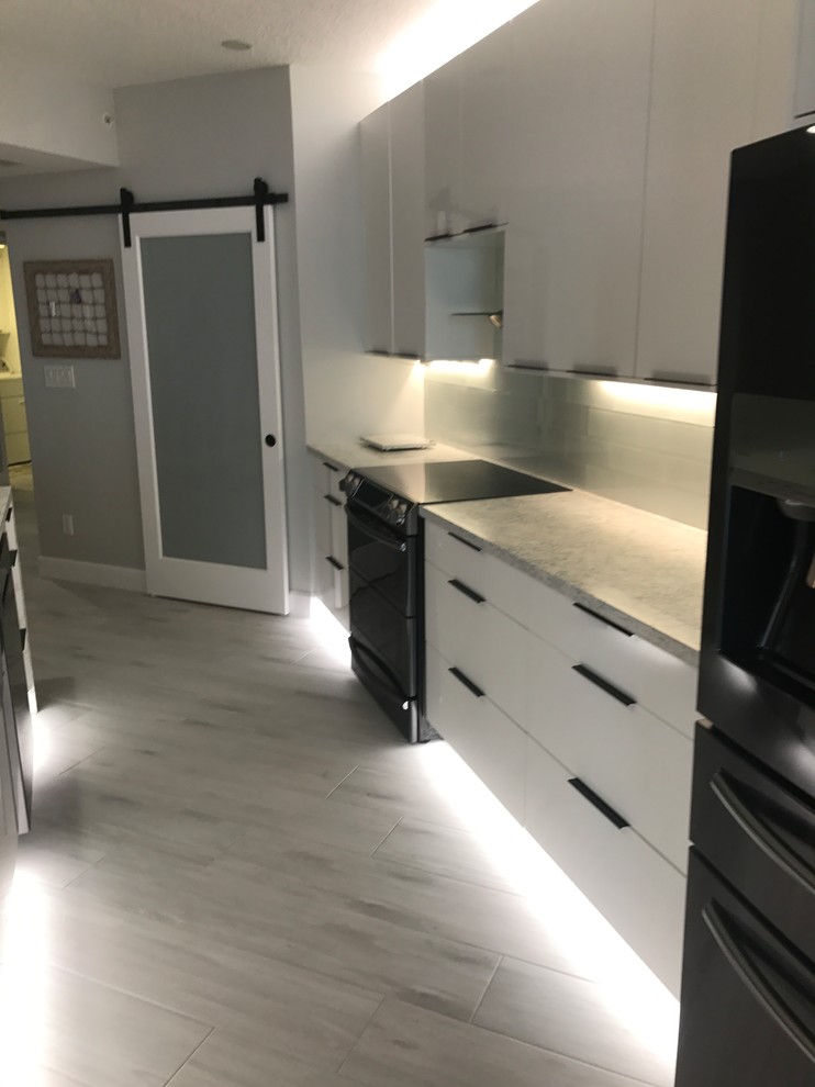 Eat-in kitchen - mid-sized contemporary galley porcelain tile and gray floor eat-in kitchen idea in Miami with a farmhouse sink, flat-panel cabinets, white cabinets, quartz countertops, white backsplash, glass tile backsplash, black appliances, an island and multicolored countertops