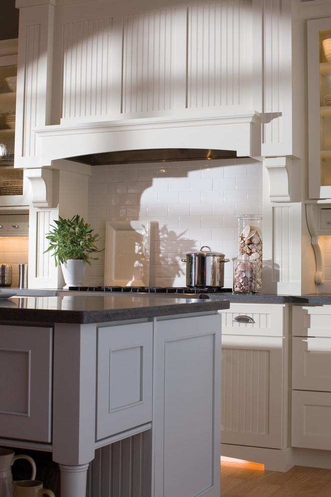 Inspiration for an eclectic light wood floor kitchen remodel in Minneapolis with a farmhouse sink, flat-panel cabinets, white cabinets, solid surface countertops, white backsplash, subway tile backsplash, stainless steel appliances and an island