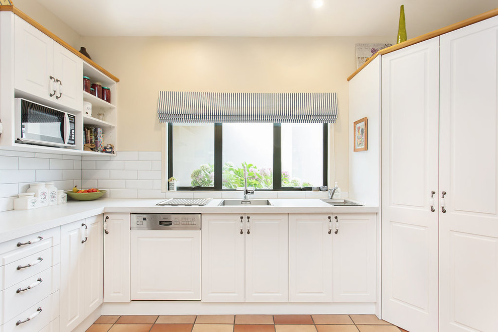 Bild på ett avskilt, litet lantligt vit vitt u-kök, med en enkel diskho, luckor med infälld panel, vita skåp, vitt stänkskydd, stänkskydd i keramik, rostfria vitvaror, klinkergolv i terrakotta och orange golv