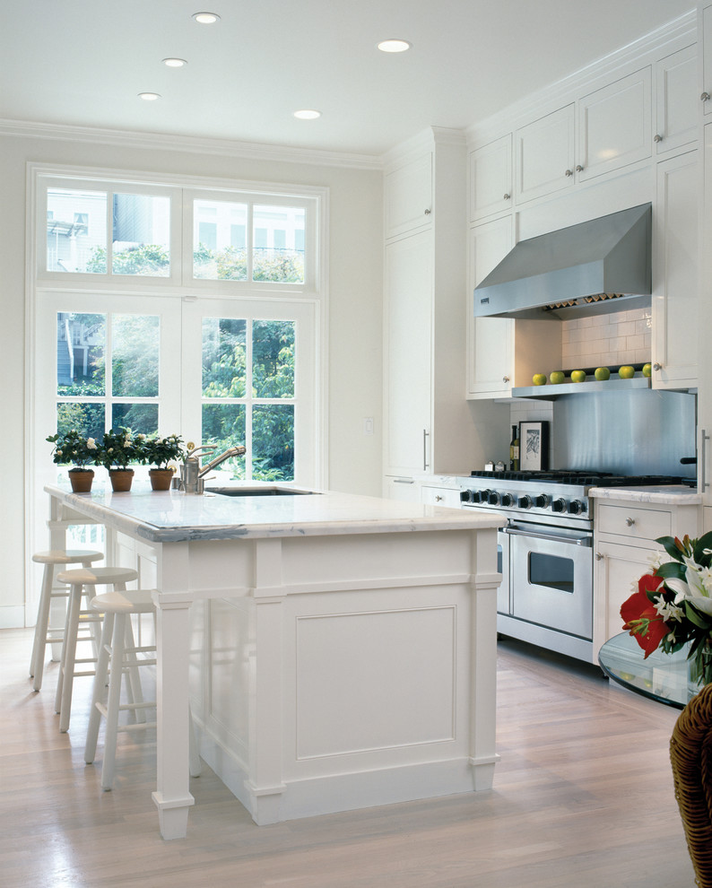 Inspiration for a classic kitchen in San Francisco with a submerged sink, shaker cabinets, white cabinets, white splashback, metro tiled splashback, stainless steel appliances and light hardwood flooring.