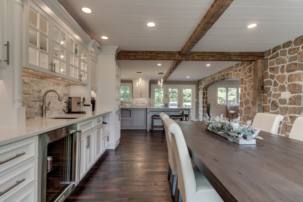 Idéer för att renovera ett lantligt vit vitt kök och matrum, med en rustik diskho, luckor med upphöjd panel, vita skåp, granitbänkskiva, vitt stänkskydd, stänkskydd i stenkakel, rostfria vitvaror, mörkt trägolv, en köksö och brunt golv