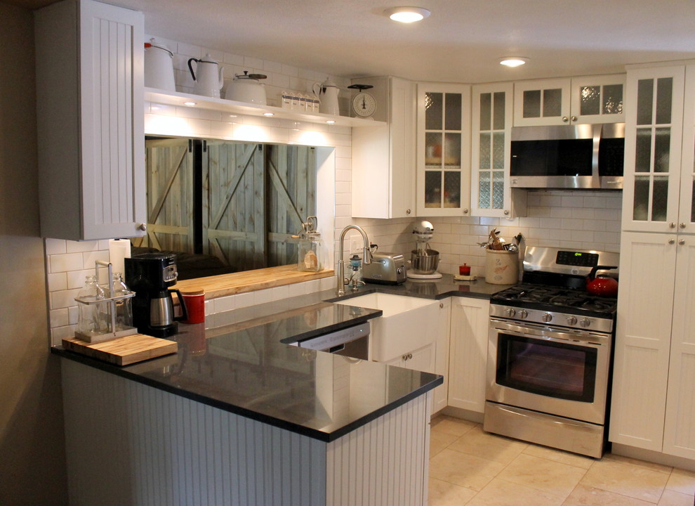 Photo of a small country u-shaped kitchen/diner in Denver with a belfast sink, beaded cabinets, white cabinets, granite worktops, white splashback, metro tiled splashback, stainless steel appliances, travertine flooring and a breakfast bar.