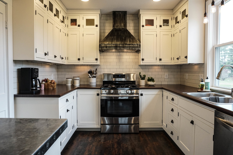 Photo of a small rural u-shaped kitchen pantry in Columbus with a built-in sink, shaker cabinets, white cabinets, white splashback, metro tiled splashback, stainless steel appliances, dark hardwood flooring, an island, brown floors and zinc worktops.