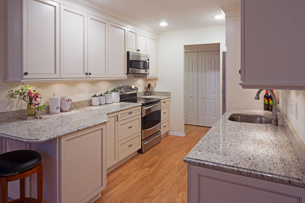 Example of a mid-sized classic galley medium tone wood floor enclosed kitchen design in Chicago with a single-bowl sink, recessed-panel cabinets, white cabinets and stainless steel appliances