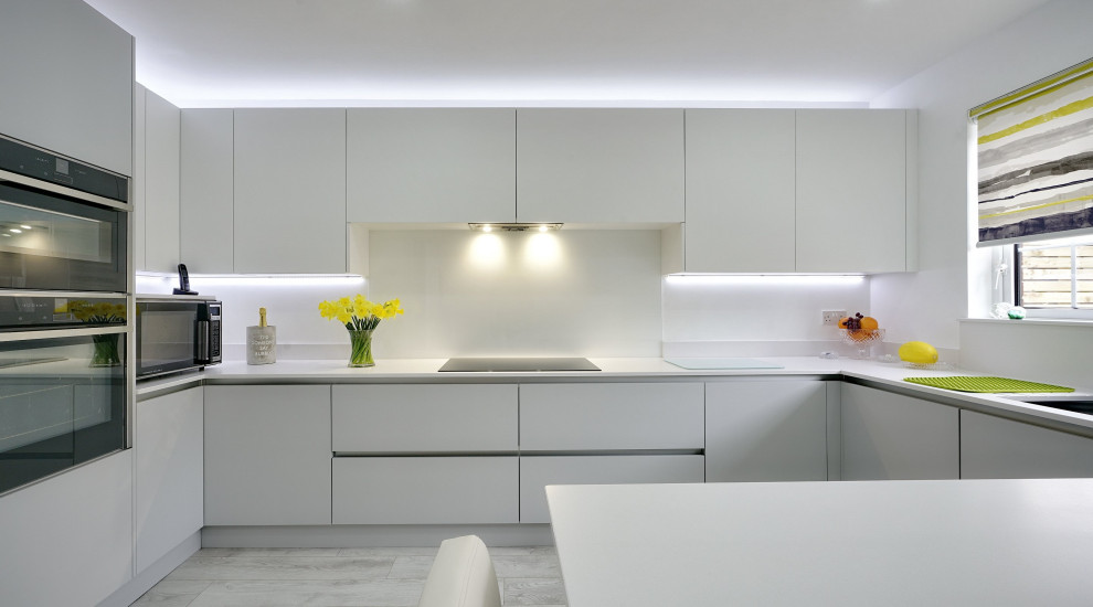 Inredning av ett modernt avskilt, mellanstort vit vitt u-kök, med en integrerad diskho, släta luckor, vita skåp, bänkskiva i kvartsit, vitt stänkskydd, svarta vitvaror, laminatgolv, en halv köksö och grått golv