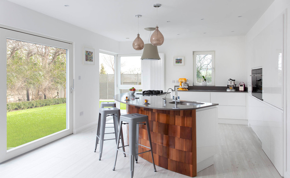 Inspiration for a large contemporary l-shaped open plan kitchen in Other with a submerged sink, flat-panel cabinets, white cabinets, quartz worktops, grey splashback, stone slab splashback, stainless steel appliances, light hardwood flooring and an island.
