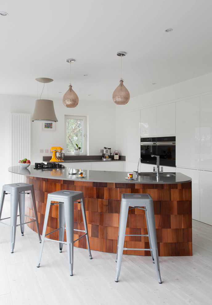 Large contemporary l-shaped open plan kitchen in Other with a submerged sink, flat-panel cabinets, white cabinets, quartz worktops, grey splashback, stone slab splashback, stainless steel appliances, light hardwood flooring and an island.