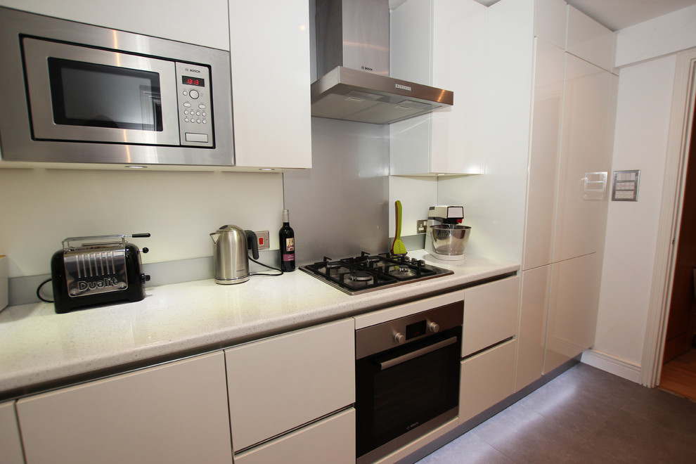 Idées déco pour une petite cuisine moderne en L fermée avec des portes de placard blanches et une crédence grise.