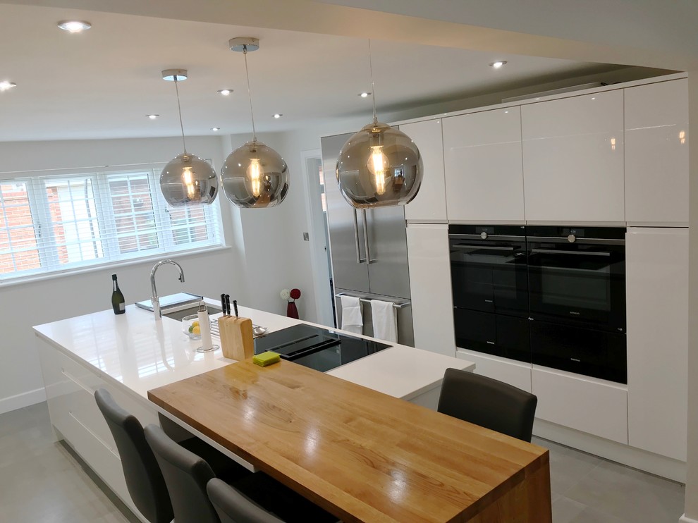 This is an example of a large contemporary galley kitchen/diner in Buckinghamshire with flat-panel cabinets, white cabinets, quartz worktops, stainless steel appliances, porcelain flooring, an island, grey floors and white worktops.