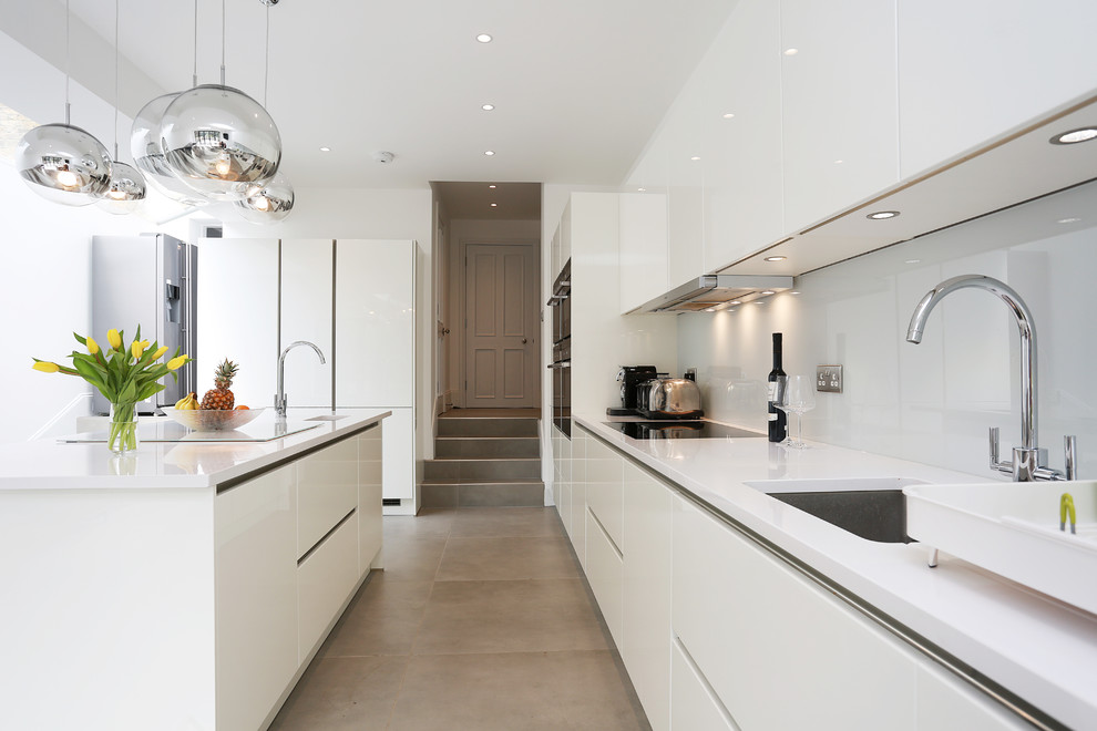 Photo of a modern kitchen in London with a single-bowl sink, glass-front cabinets, white cabinets, grey splashback, glass sheet splashback, stainless steel appliances and an island.