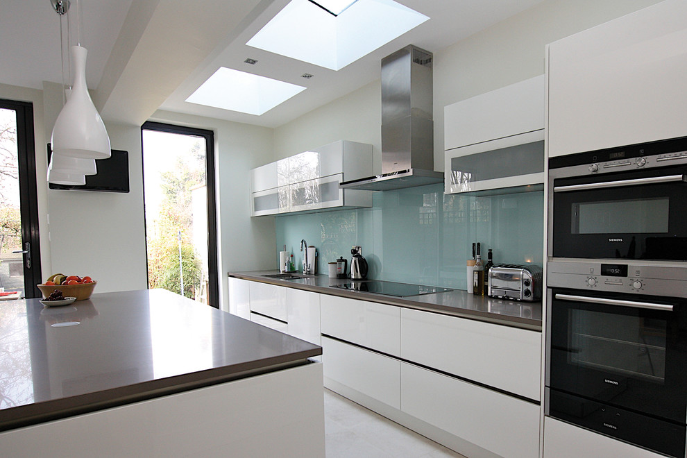 Contemporary kitchen in London with white cabinets, engineered stone countertops, stainless steel appliances and an island.