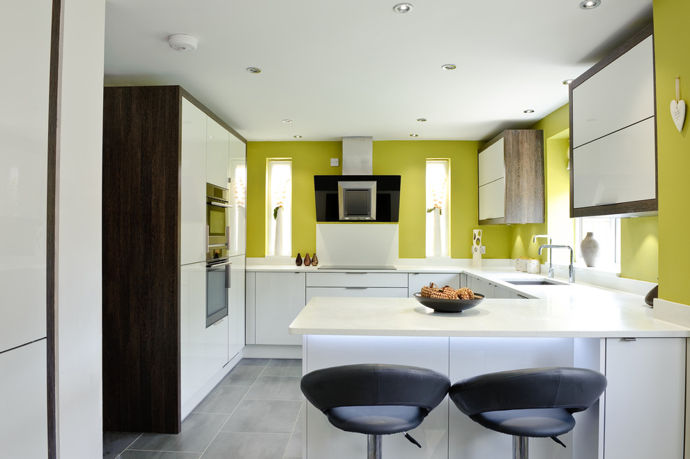 Photo of a contemporary u-shaped kitchen in Kent with a submerged sink, flat-panel cabinets, white cabinets, integrated appliances, slate flooring and no island.