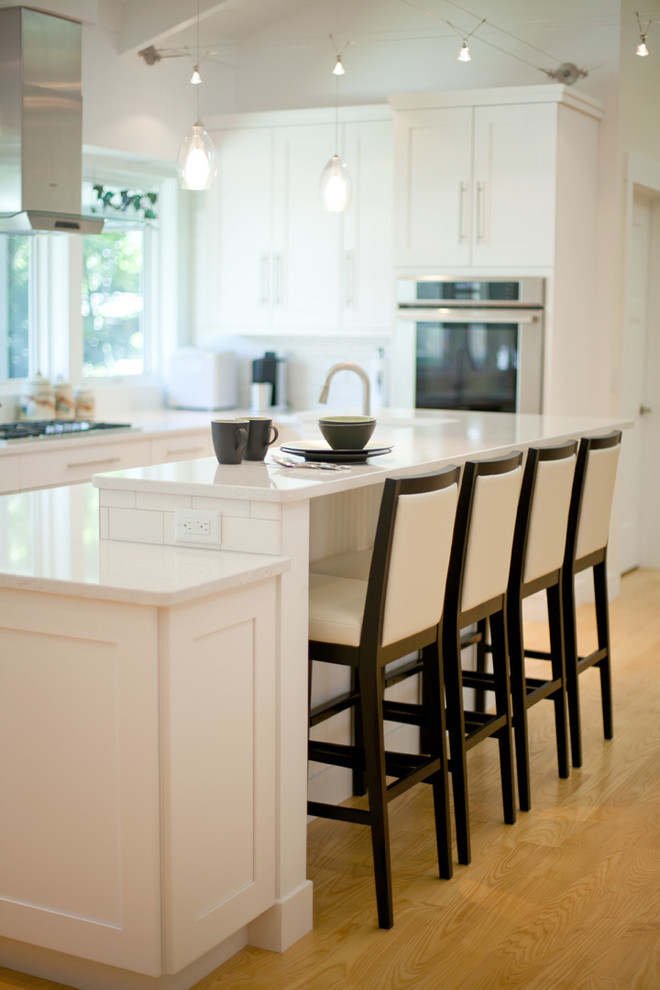 Imagen de cocina contemporánea con fregadero bajoencimera, armarios estilo shaker, puertas de armario blancas, encimera de cuarzo compacto, salpicadero blanco, salpicadero de azulejos tipo metro, electrodomésticos de acero inoxidable y suelo de madera clara