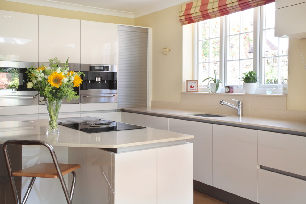 Foto på ett stort funkis kök, med släta luckor, vita skåp, bänkskiva i kvartsit, rostfria vitvaror, mellanmörkt trägolv, en köksö och en undermonterad diskho