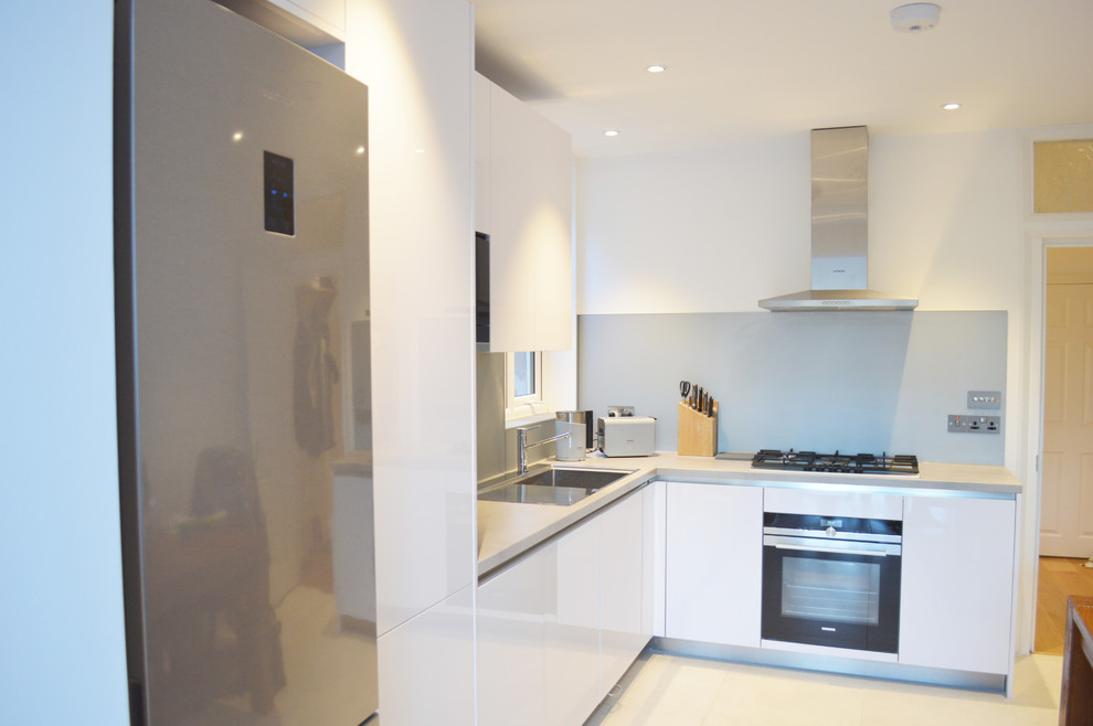 Foto på ett mellanstort funkis kök, med en nedsänkt diskho, luckor med profilerade fronter, vita skåp, laminatbänkskiva, blått stänkskydd, stänkskydd i glaskakel och svarta vitvaror