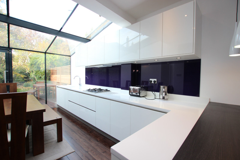 Modern kitchen in London with white cabinets, a breakfast bar and dark hardwood flooring.