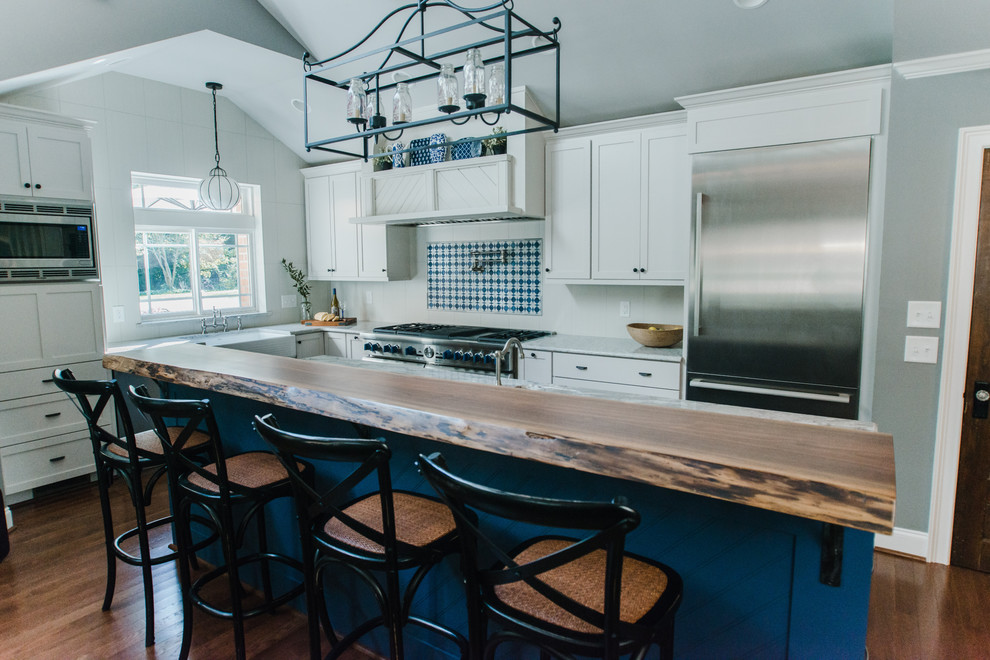 Inspiration for a large transitional l-shaped medium tone wood floor and brown floor eat-in kitchen remodel in Charlotte with a farmhouse sink, shaker cabinets, white cabinets, granite countertops, white backsplash, ceramic backsplash, stainless steel appliances, an island and gray countertops
