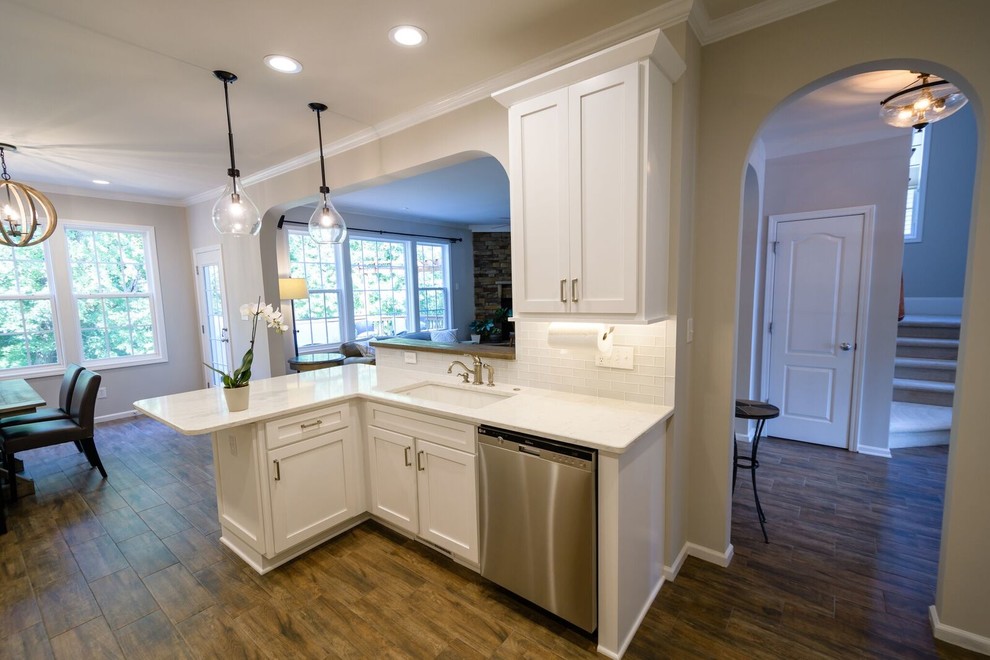 Inspiration for a mid-sized transitional u-shaped medium tone wood floor and brown floor eat-in kitchen remodel in Raleigh with an undermount sink, shaker cabinets, white cabinets, quartzite countertops, white backsplash, glass tile backsplash, stainless steel appliances and a peninsula