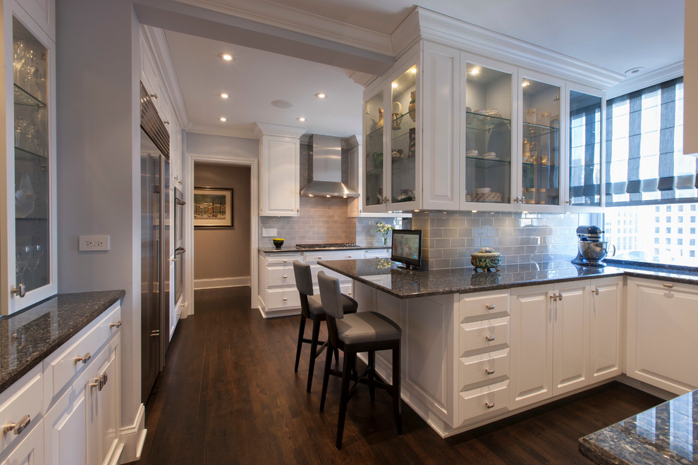 Design ideas for a traditional enclosed kitchen in Chicago with a submerged sink, glass-front cabinets, white cabinets, granite worktops, blue splashback, glass sheet splashback, stainless steel appliances and dark hardwood flooring.