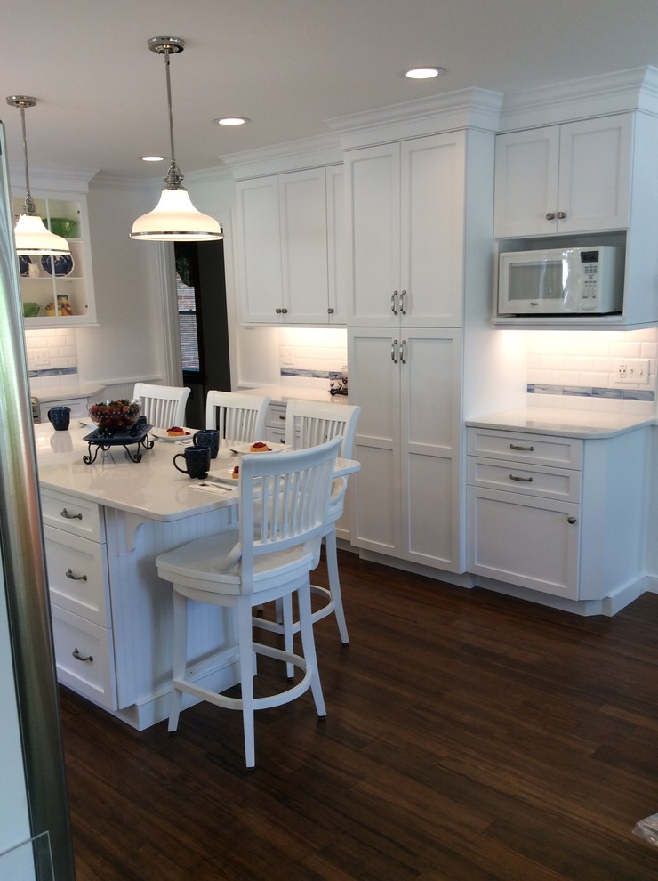 Mid-sized cottage u-shaped bamboo floor eat-in kitchen photo in Other with a farmhouse sink, shaker cabinets, white cabinets, quartz countertops, white backsplash, porcelain backsplash, stainless steel appliances and an island