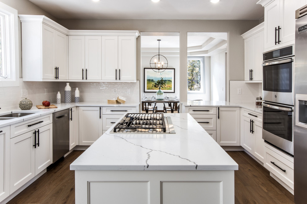This is an example of a medium sized traditional kitchen/diner in Denver with a submerged sink, shaker cabinets, white cabinets, engineered stone countertops, white splashback, metro tiled splashback, stainless steel appliances, medium hardwood flooring, an island, brown floors and white worktops.