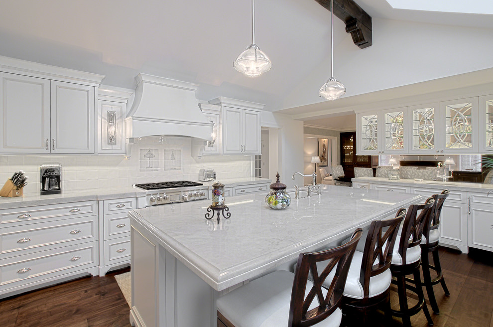 This is an example of a large traditional l-shaped kitchen/diner in Chicago with recessed-panel cabinets, white cabinets, quartz worktops, white splashback, ceramic splashback, dark hardwood flooring, an island, stainless steel appliances, brown floors, white worktops and a vaulted ceiling.