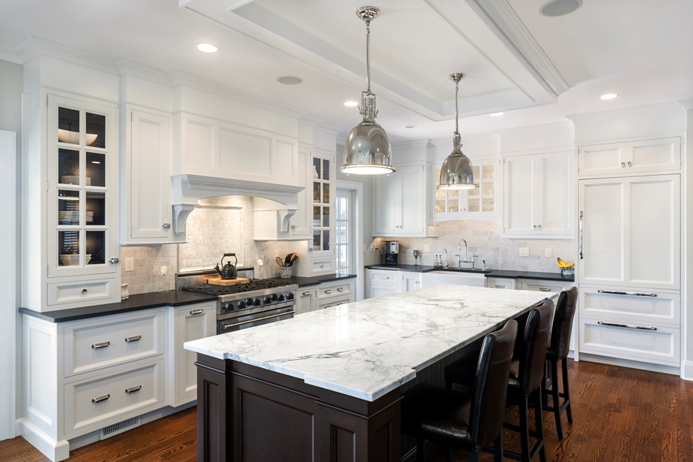 Large transitional l-shaped medium tone wood floor eat-in kitchen photo in New York with a farmhouse sink, shaker cabinets, white cabinets, marble countertops, gray backsplash, an island, stone tile backsplash and paneled appliances