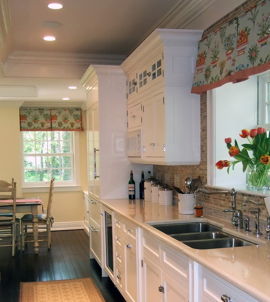 Exemple d'une cuisine américaine chic avec un placard avec porte à panneau encastré, un évier 3 bacs, des portes de placard blanches, une crédence marron et une crédence en mosaïque.