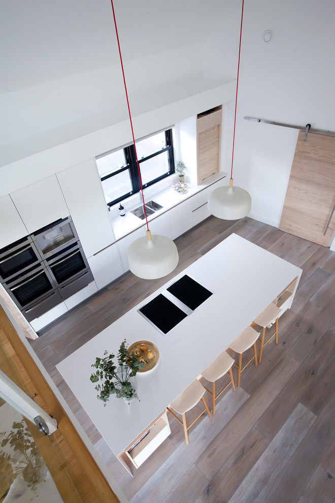 Modern inredning av ett kök, med en undermonterad diskho, släta luckor, vita skåp, bänkskiva i kvartsit, ljust trägolv och en köksö