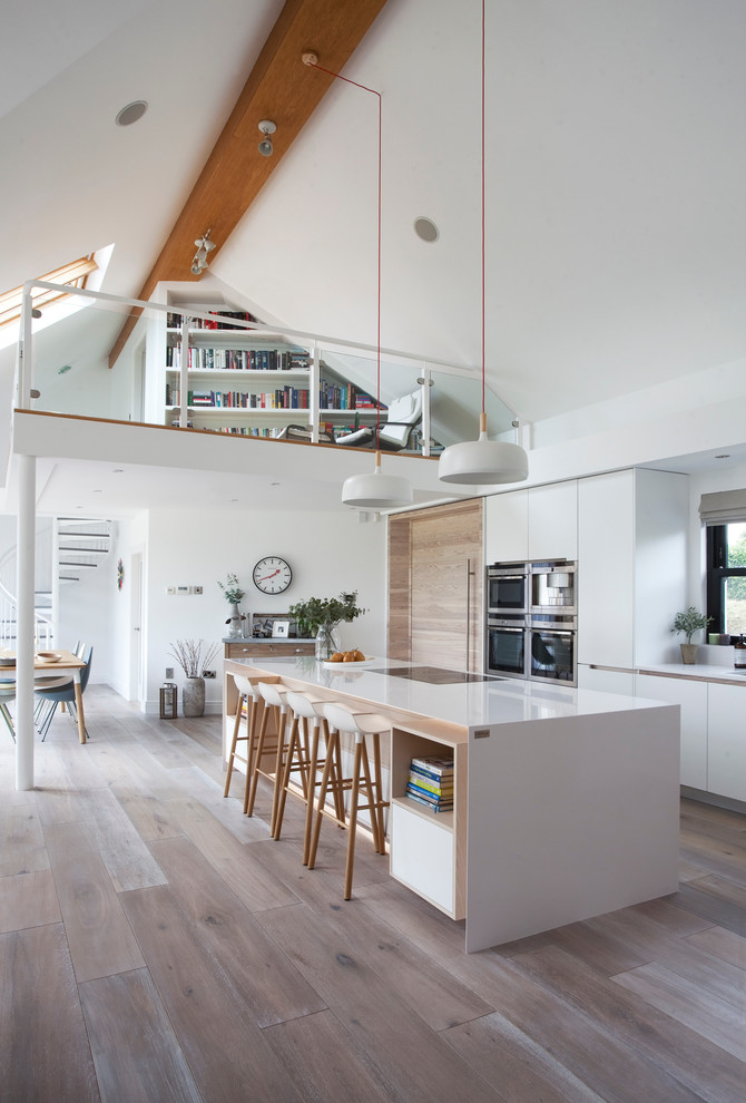 Contemporary galley kitchen/diner in Other with a submerged sink, flat-panel cabinets, white cabinets, quartz worktops, light hardwood flooring and an island.