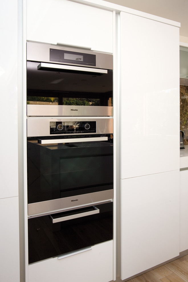 Ejemplo de cocina contemporánea con armarios con paneles lisos, puertas de armario blancas y electrodomésticos de acero inoxidable