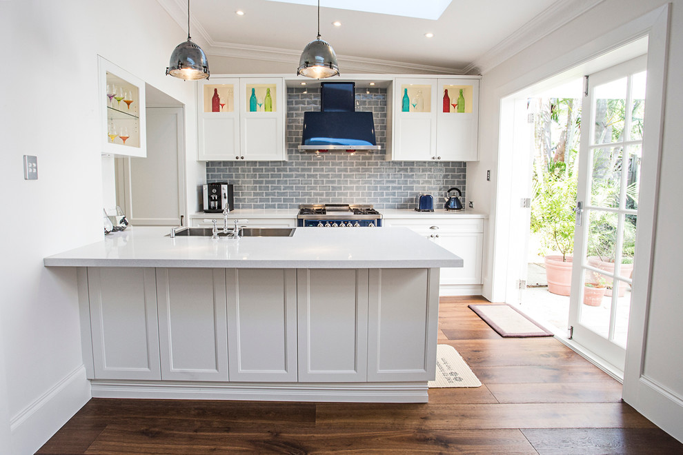 Medium sized contemporary l-shaped kitchen/diner in Other with a submerged sink, flat-panel cabinets, white cabinets, engineered stone countertops, grey splashback, glass tiled splashback, stainless steel appliances, medium hardwood flooring and an island.