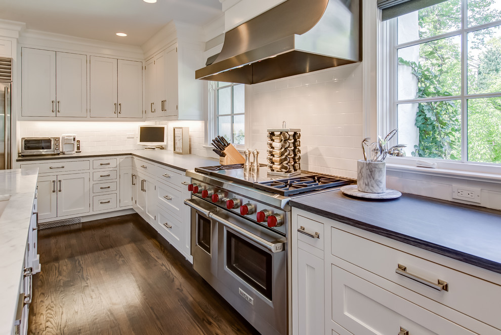 This is an example of a large classic l-shaped open plan kitchen in New York with a built-in sink, shaker cabinets, white cabinets, engineered stone countertops, white splashback, metro tiled splashback, stainless steel appliances, dark hardwood flooring, an island and brown floors.
