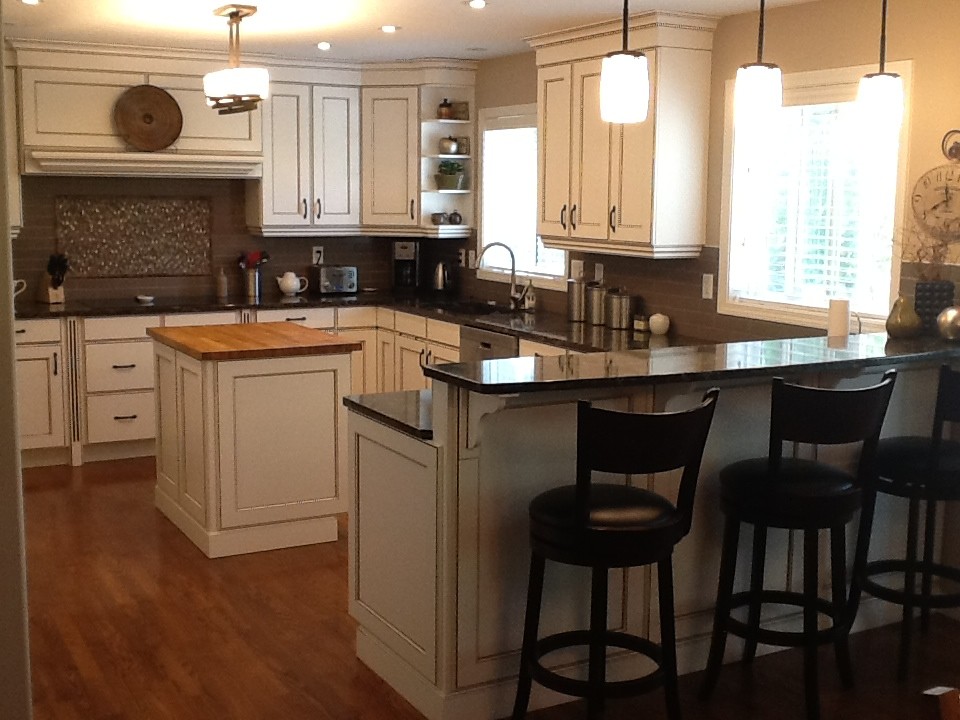 Photo of a medium sized rustic u-shaped kitchen/diner in Calgary with recessed-panel cabinets, white cabinets, brown splashback, metro tiled splashback, stainless steel appliances, medium hardwood flooring, an island and a submerged sink.