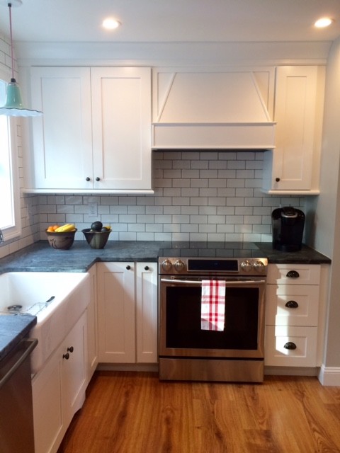 This is an example of a medium sized rural u-shaped kitchen/diner in New York with a belfast sink, shaker cabinets, white cabinets, soapstone worktops, white splashback, metro tiled splashback, stainless steel appliances, medium hardwood flooring and a breakfast bar.