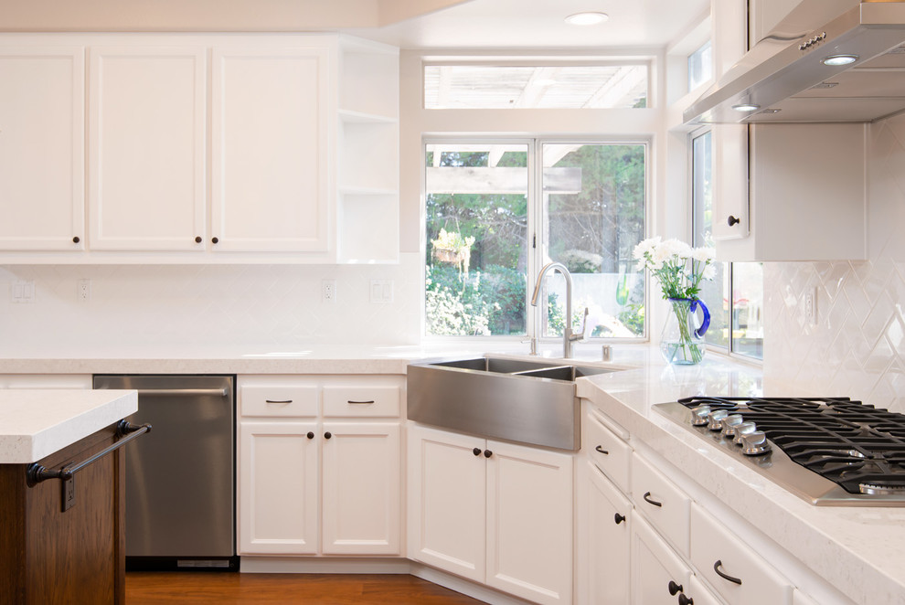 Moderne Küche mit Doppelwaschbecken, weißen Schränken, Küchenrückwand in Weiß, Küchengeräten aus Edelstahl, Kücheninsel und braunem Boden in San Diego
