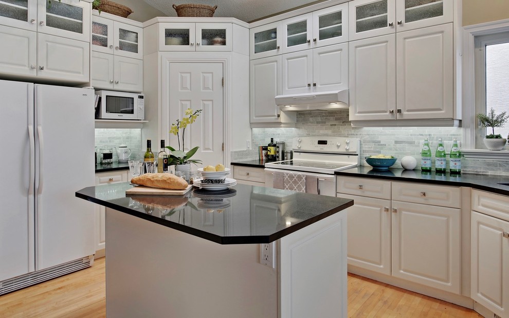 Small elegant u-shaped light wood floor kitchen pantry photo in Other with an integrated sink, raised-panel cabinets, white cabinets, quartz countertops, gray backsplash, white appliances, an island and stone tile backsplash