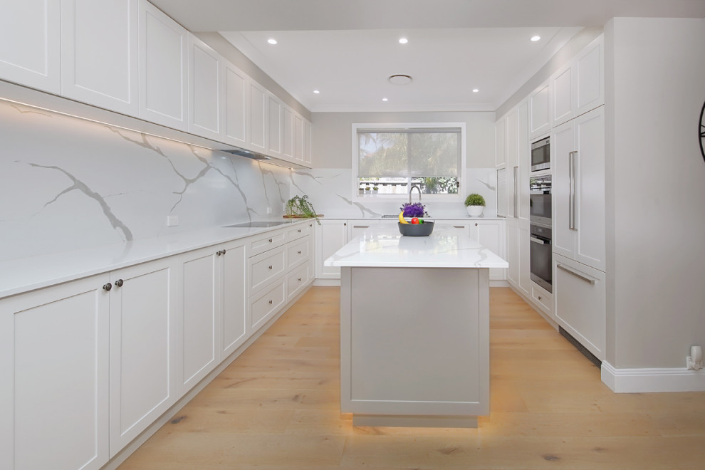 This is an example of a large modern u-shaped kitchen/diner in Sydney with an integrated sink, raised-panel cabinets, white cabinets, engineered stone countertops, white splashback, stone slab splashback, integrated appliances, dark hardwood flooring, an island, brown floors and white worktops.