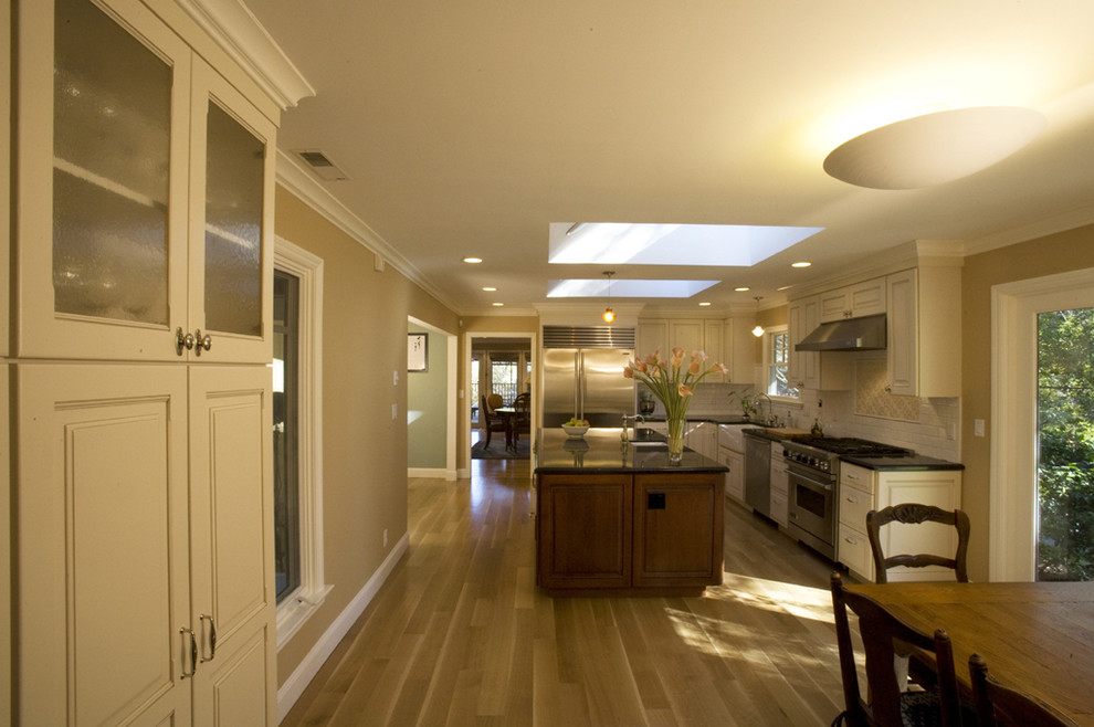Large elegant l-shaped light wood floor eat-in kitchen photo in San Francisco with subway tile backsplash, stainless steel appliances, a farmhouse sink, raised-panel cabinets, white cabinets, granite countertops, white backsplash and an island