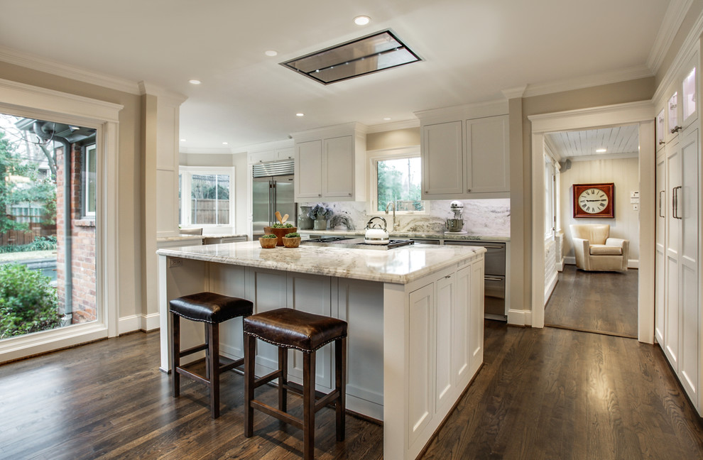 Large transitional u-shaped dark wood floor eat-in kitchen photo in Dallas with a farmhouse sink, shaker cabinets, white cabinets, marble countertops, white backsplash, stone slab backsplash, stainless steel appliances and an island