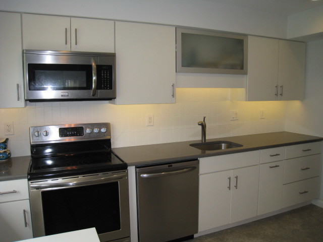 Exempel på ett mellanstort 50 tals kök, med en undermonterad diskho, släta luckor, vita skåp, granitbänkskiva, vitt stänkskydd, stänkskydd i tunnelbanekakel, rostfria vitvaror, travertin golv och en köksö