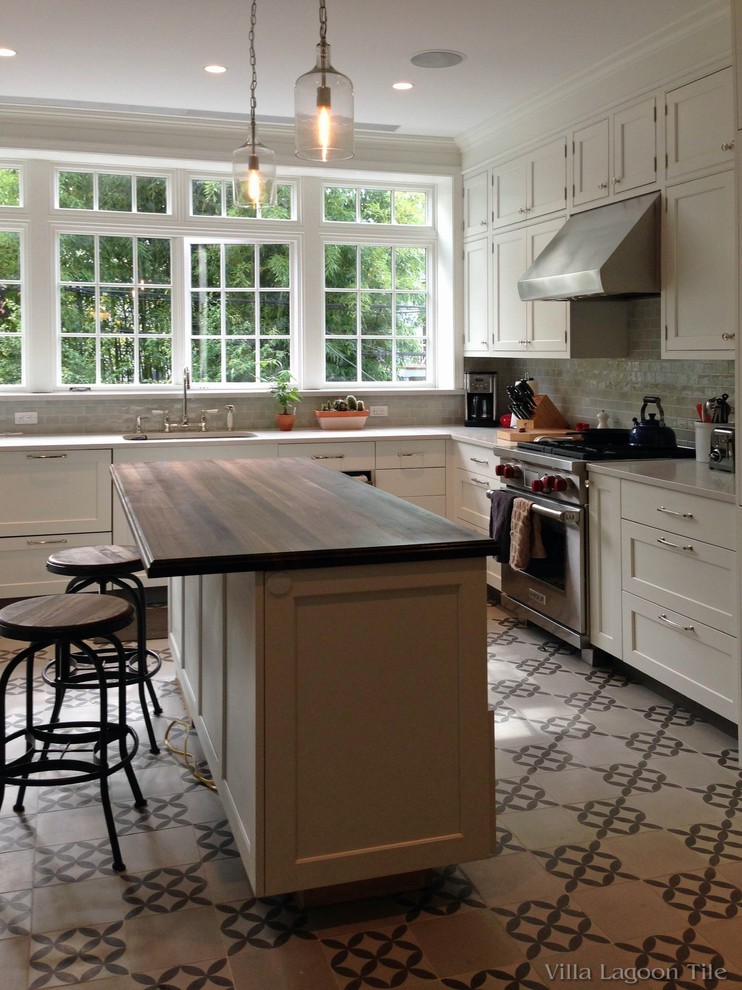 Lantlig inredning av ett mellanstort kök, med en undermonterad diskho, luckor med infälld panel, vita skåp, träbänkskiva, grått stänkskydd, stänkskydd i keramik, rostfria vitvaror, cementgolv, en köksö och flerfärgat golv