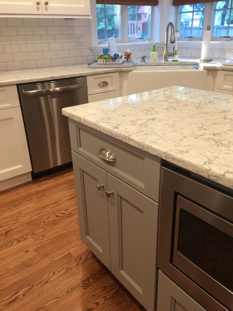 Medium sized traditional u-shaped kitchen/diner in New York with a belfast sink, shaker cabinets, white cabinets, engineered stone countertops, white splashback, porcelain splashback, stainless steel appliances, light hardwood flooring and brown floors.